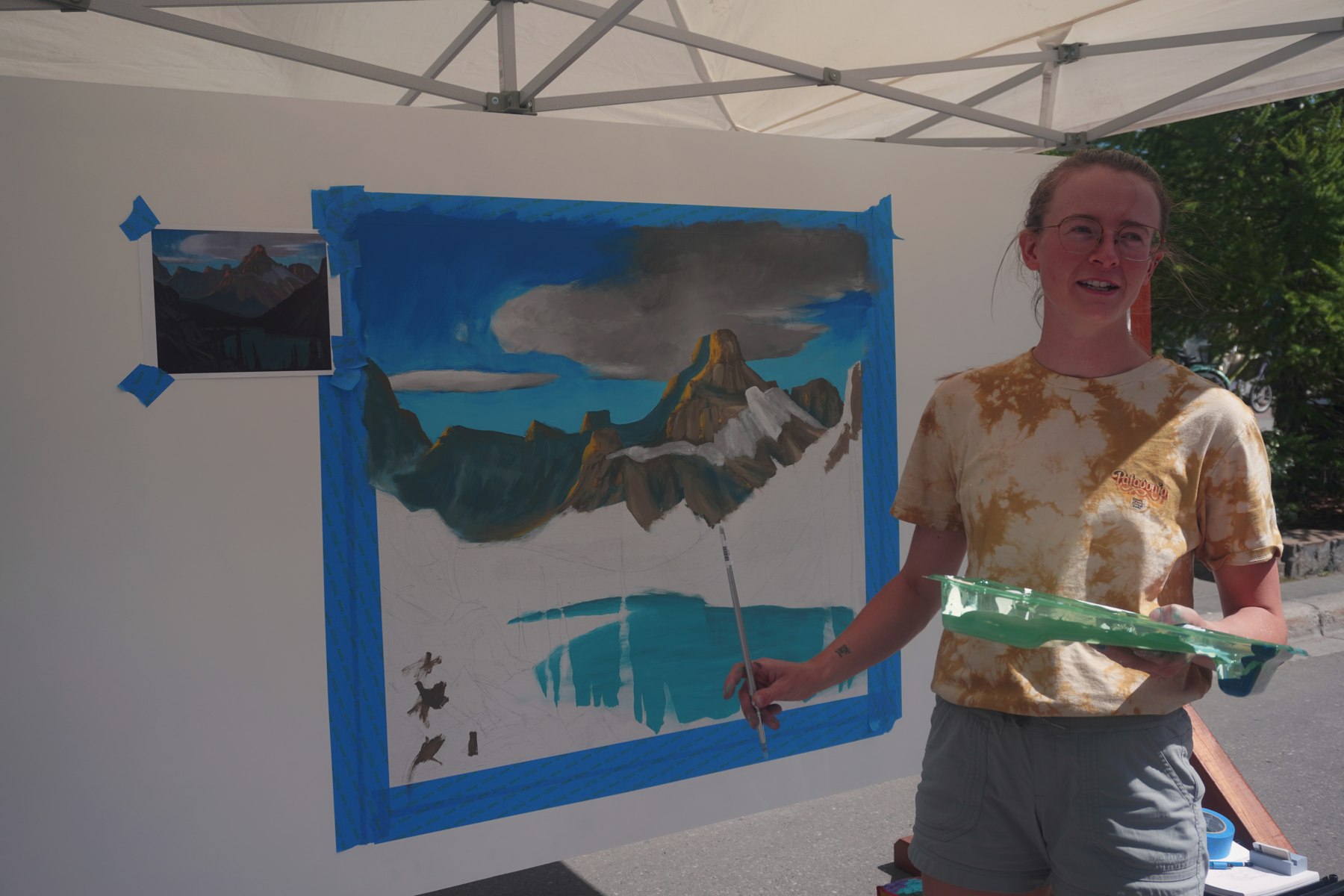 An artist painting a mountain landscape at an outdoor art display