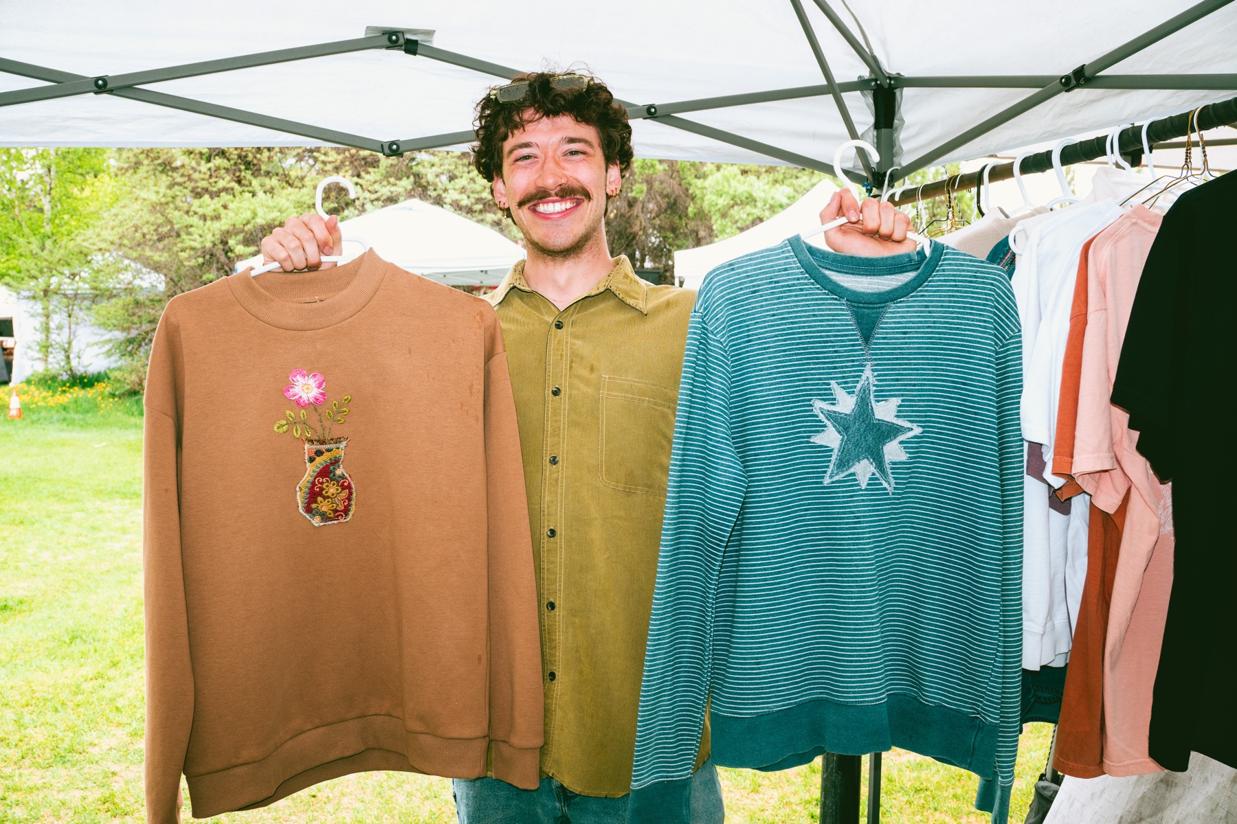 An artist holding handmade sweaters at a market stall