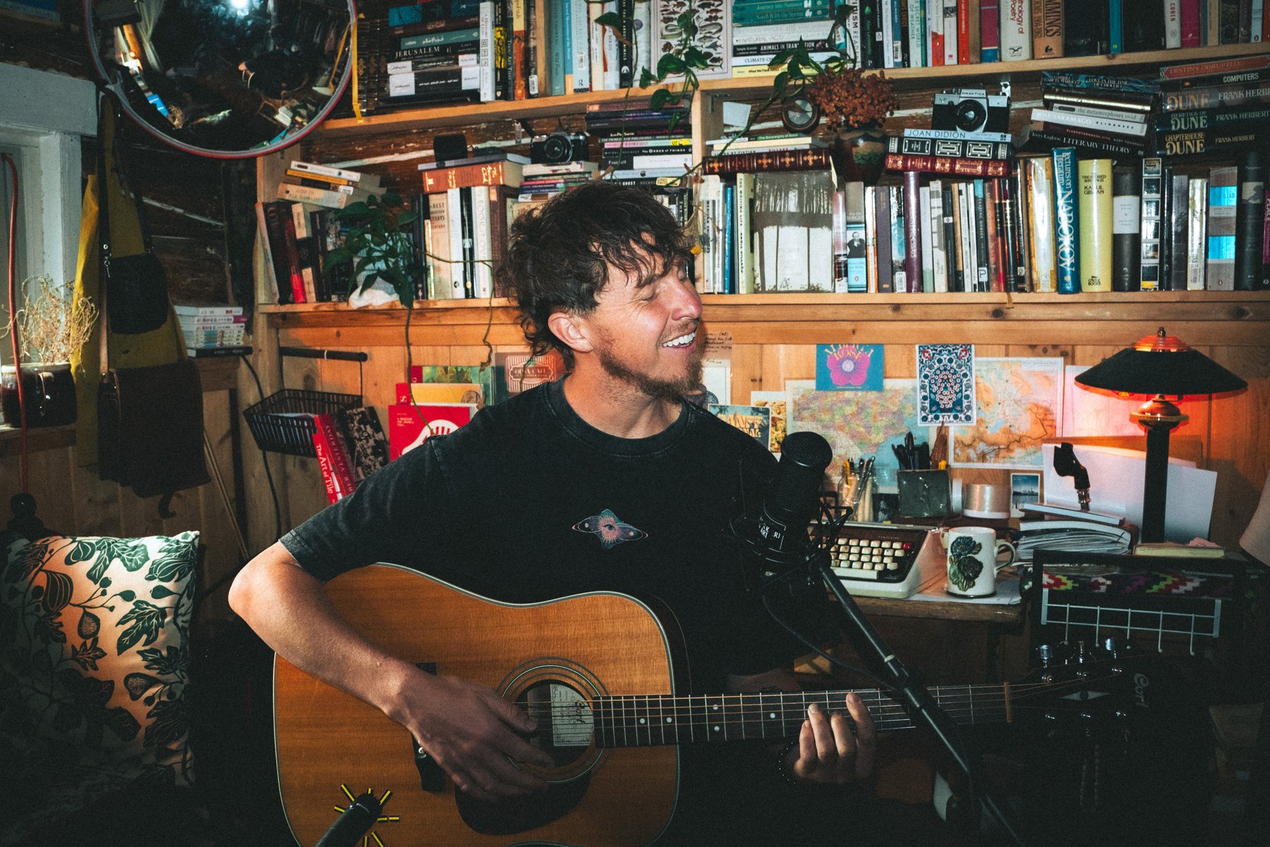 A musician playing guitar in a room lined with books